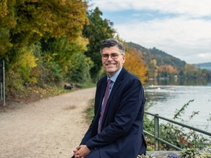 Landrat Kistler Copyright Ornella Cacace: Auf dem Bild ist Landrat Dr. Martin Kistler zu sehen, wie er am Rheinuferweg auf einer Bank sitzt. Im Hintergrund ist rechts der Rhein und links der Uferweg mit Bumen und Struchern zu sehen, die vom Herbst bunt gefrbt sind.